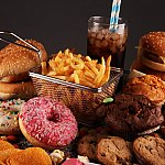 A variety of unhealthy ultra-processed foods, including donuts, potato chips, fries, waffles, and processed fish sandwich.