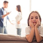 Sad little girl looks straight ahead while her parents are arguing in the background. 
