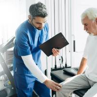 Health professional examining senior man’s knee.