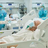 Healthcare worker wheeling hospital bed with senior COVID-19 patient on ventilator