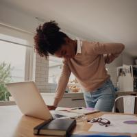 Young woman standing and holding back while working on laptop at home