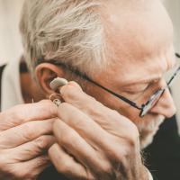 Older man places a hearing aid in his ear. 