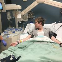 A medical technician watches the monitor of a woman with IVs in a hospital bed.