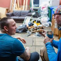 Rear view of two men wearing construction uniforms sitting down for a lunch break at a building renovation site.
