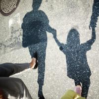 Shadow of two adults walking on a crosswalk and holding hands with a young child in between them.