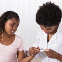 A doctor uses a glucometer to check a young patient’s glucose level in a hospital examination room