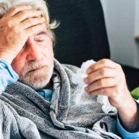 Older man holding his head with one hand and a tissue in the other