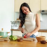 Woman cutting a tomato to make a salad in the kitchen.