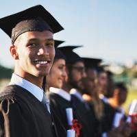 Smiling adults in graduate attire stand shoulder-to-shoulder.