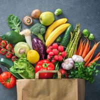 An assortment of fruits and vegetables spilling out of a paper grocery bag