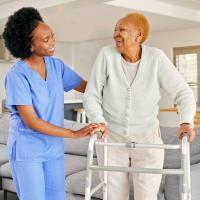 A health care worker helping an older adult woman with a walker