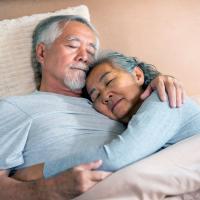 An older adult couple embracing while sleeping in bed
