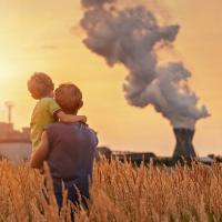 A father holding his son while looking at a smokestack in the distance