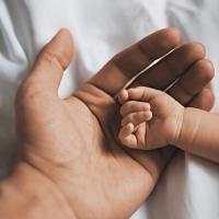 An infant's hand laying on top of a parent's hand.