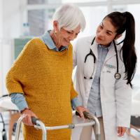 Doctor and elderly woman using a walker for support.