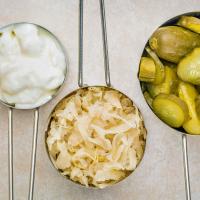 Three measuring cups with yogurt, sauerkraut, and pickles.