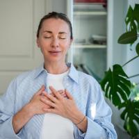 A woman standing in her home with her hands on her chest and eyes closed, enjoying the clean air.
