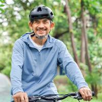 An older man riding a bicycle on a path in the woods.
