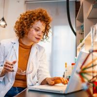 Biologist sitting at a lab table, looking at the laptop screen while studying test results.