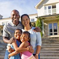 A smiling family of four standing in front of their house.
