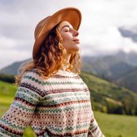 A woman standing outdoors with her eyes closed and arms out.
