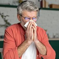 A man sneezing into a tissue in a kitchen.