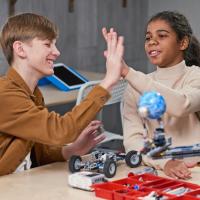 Two teenagers high-fiving while building a robot.