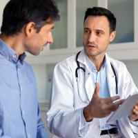 A male patient talking with a doctor holding a tablet.