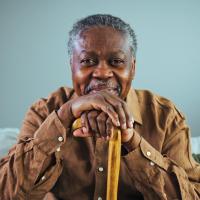 An older man sitting on a couch, holding a cane.