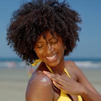 A woman at the beach applying sunscreen to her shoulder.