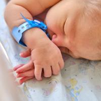A newborn baby with a maternity hospital bracelet sleeping in a clinic crib.