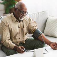 African American Male measuring blood pressure sitting on a couch at home.