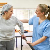 An older woman in rehabilitation therapy practicing walking with a caregiver.
