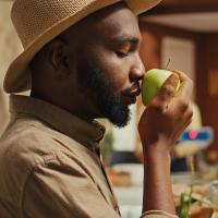 A man smelling a green apple in a kitchen.