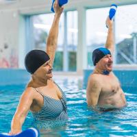 A senior man and woman exercising in an indoor swimming pool.