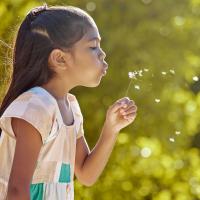 A young girl blowing dandelion seeds outdoors.