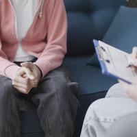 Doctor writing notes on clipboard, sitting near young patient, teen counselling 