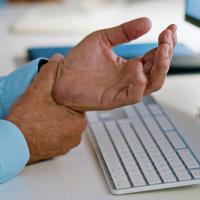 A close-up of a man holding his wrist while sitting at a desk.