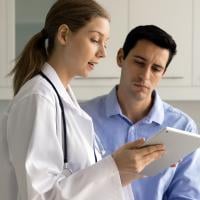 A female doctor showing a male patient information on a tablet during an appointment.