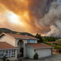 A home with thick wildfire smoke filling the sky in the background.