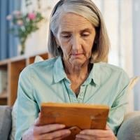 An older woman looking at a framed photograph while sitting in a chair.