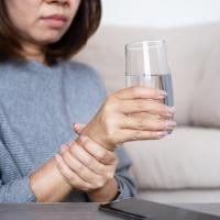 Woman holds a glass of water in one hand and uses her other hand to steady her movements. 
