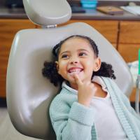 Young child smiles, pointing to her teeth, during dental checkup.