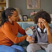 A woman comforting a teenager looking at their reflection in a mirror.
