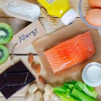 An assortment of foods commonly associated with food allergies arranged around a tag reading “Allergy.”