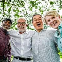 A group of smiling older adults standing together outdoors with their arms around each other.