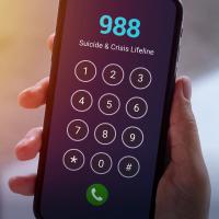 A close-up of a hand holding a smartphone displaying the 988 Suicide & Crisis Lifeline number.