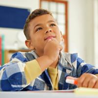 A young boy sitting at a classroom desk, looking distracted.