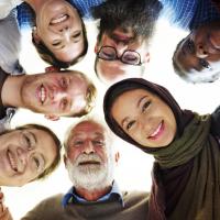 A diverse group of people of different ages and backgrounds smiling while looking down at the camera.